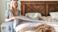 a woman standing in front of a bed with pillows and blankets on top of it