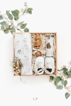 an open box containing baby's shoes, diapers and other items with greenery