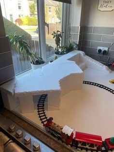 a model train set sitting on top of a counter next to a window with potted plants