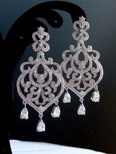 a pair of silver earrings with crystal drops on it's earring hooks, hanging from a black stand