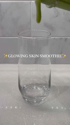 a clear glass sitting on top of a counter next to a green plant with the words glowing skin smoothie above it