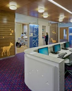 an office with two desks and computers on the counter in front of people looking at them