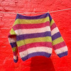 a colorful sweater hanging on a clothesline against a red wall with a white and blue stripe