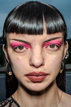 a woman with bright pink makeup and piercings on her face is looking at the camera