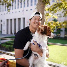 a man sitting on a bench holding a dog in his lap and smiling at the camera