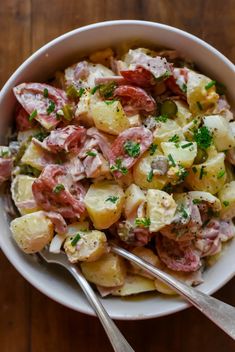 a bowl filled with potato salad and two silver spoons on top of a wooden table