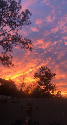 the sun is setting over some trees and lawn chairs in front of a wooden fence