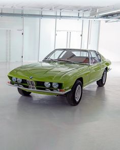 an old green car is parked in a large room with white walls and flooring