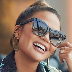 a woman wearing sunglasses is smiling and talking on her cell phone while looking at the camera