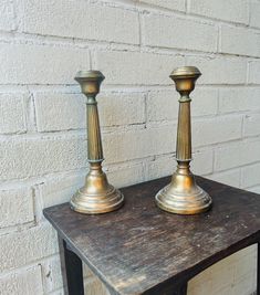 two metal candlesticks sitting on top of a wooden table next to a brick wall