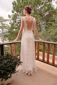 a woman in a wedding dress looking out over the balcony at trees and water on a cloudy day