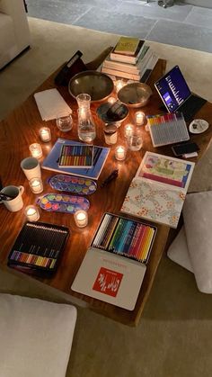 a coffee table filled with lots of books and art supplies next to candles on the floor