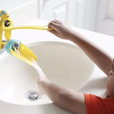 someone is washing their hands with yellow toothbrushes in the bathroom sink while another person looks on