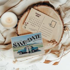 a save the date postcard next to a candle and a card on top of a wooden slice