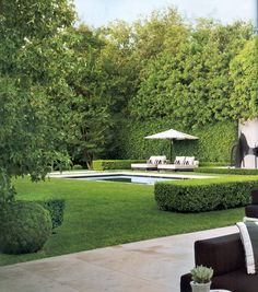 an outdoor living area with green grass and trees in the back ground, surrounded by hedges