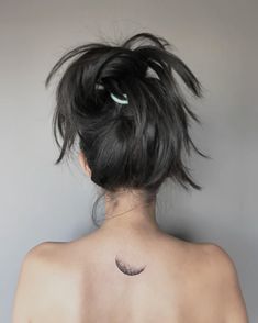 the back of a woman's neck with a small crescent tattoo on her left shoulder