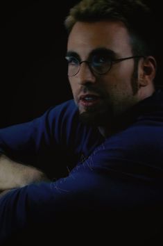 a man with glasses sitting in the dark