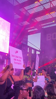 a group of people holding up signs in front of a crowd at a concert with purple lighting