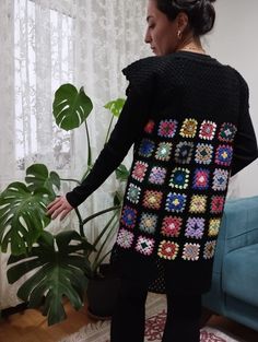 a woman standing in front of a window wearing a black sweater with multicolored squares on it