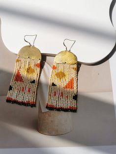 two pairs of beaded earrings on a metal stand against a white wall with shadow