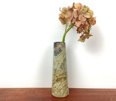 a vase with flowers in it sitting on a wooden table next to a white wall