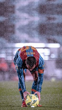 a man bending over with his foot on a soccer ball in the rain at a stadium