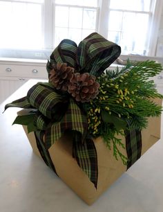 a present wrapped in brown paper with pine cones and greenery sits on a kitchen counter