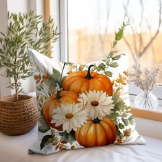 a pillow with flowers and pumpkins sitting on a window sill next to a potted plant