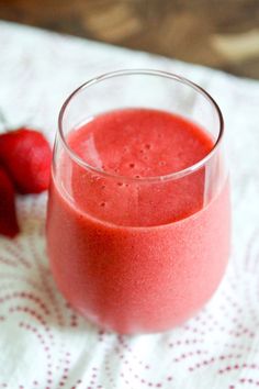 a glass filled with red liquid next to some strawberries