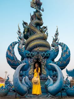 a woman in a yellow dress standing next to a blue and gold dragon sculpture with her hand on her hip