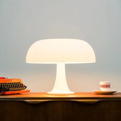 a lamp sitting on top of a wooden table next to a cup and typewriter