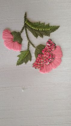 two pink flowers with green leaves on a white cloth covered tablecloth, one is stitched and the other has sequins