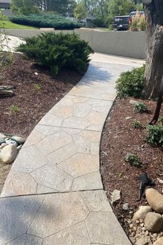 a stone walkway in front of a tree and some rocks on the side of the road