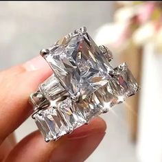 someone is holding an engagement ring that has three princess cut diamonds on each side and two baguettes in the middle