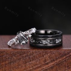 two wedding rings with black and white diamonds on top of each other, sitting on a wooden surface