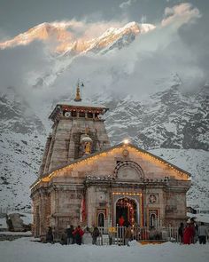 a group of people standing in front of a building with snow on the mountains behind it