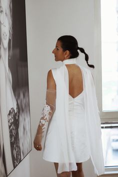 a woman standing in front of a painting and wearing a white dress with sheer sleeves