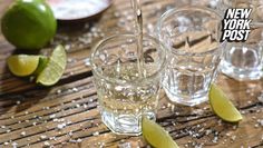 three shot glasses filled with water and limes on a wooden table next to two lime wedges