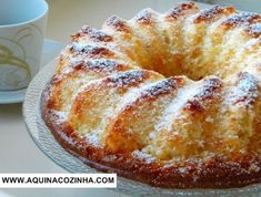 a bundt cake with powdered sugar on top sits on a plate next to a cup and saucer