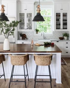 a kitchen with white cabinets and wooden counter tops next to two stools in front of an island