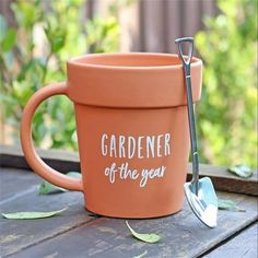 an orange flower pot sitting on top of a wooden table next to a gardening utensil