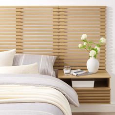 a white vase with flowers sitting on top of a bed next to a wooden headboard