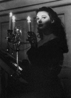 black and white photograph of a woman holding a chandelier with candles in the background