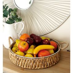 a basket filled with assorted fruit next to a white vase on top of a wooden table