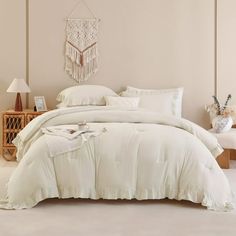 a bed with white comforter and pillows in a room next to a lamp on a table