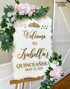 a welcome sign with flowers and greenery on it in front of a white wall