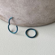 two blue hoop earrings sitting on top of a white table next to a stone wall