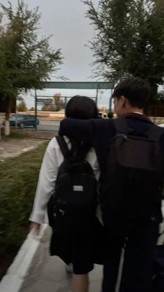 two people walking down a sidewalk with backpacks on their back and one person holding the other's arm