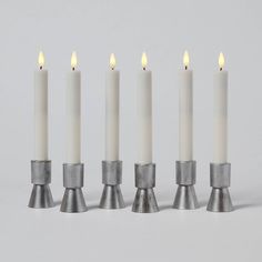 four white candles are lined up in a row with one candle on the other side