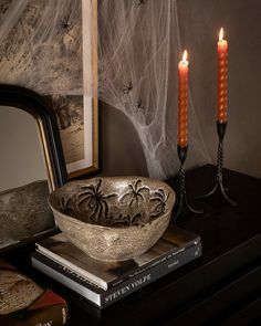 a bowl with two candles sitting on top of a table next to books and a mirror